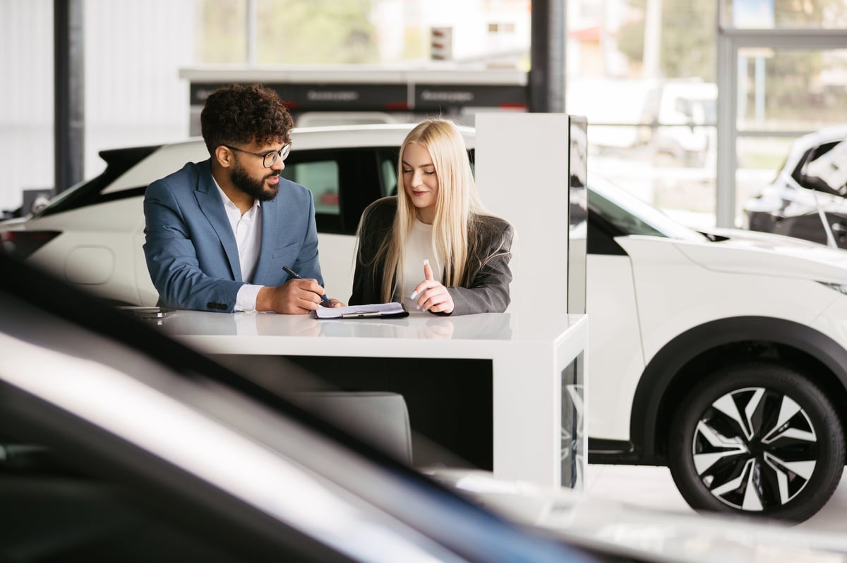 Salesman and female customer discussing car buying agreement at a dealership desk. Focusing on professional consultation and informed decision-making